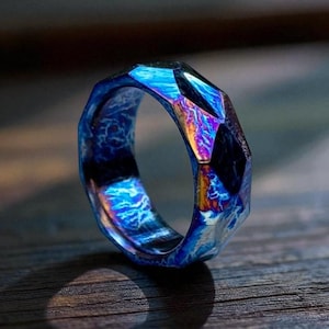 May include: A faceted ring with a vibrant, iridescent finish. The ring's surface displays a spectrum of colors, including blues, purples, and hints of gold. The design features a geometric pattern, creating a unique and eye-catching piece of jewelry.