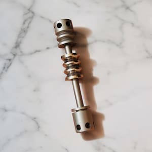 May include: A metallic, cylindrical tool with a series of stacked, ridged sections and two rounded ends, each with multiple holes. The central section is a contrasting gold color, and the tool has a sleek, industrial design.