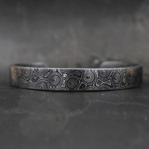 Puede incluir: Una pulsera de plata con un patrón de espiral. La pulsera está hecha de metal y tiene un acabado pulido.