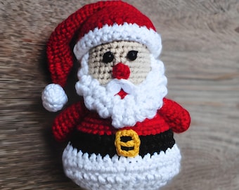 May include: Crocheted Santa Claus ornament with a red hat, white beard, and black belt. The ornament is made of yarn and has a white pom-pom on the hat.
