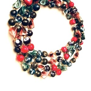 May include: A multi-strand necklace made of colorful glass beads. The beads are in shades of red, green, blue, and black. Some of the beads are round, while others are triangular.