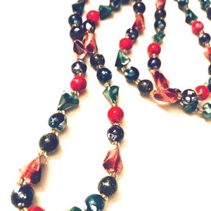 May include: A long necklace made of black, green, and red beads. The beads are various shapes and sizes, including round and triangular.