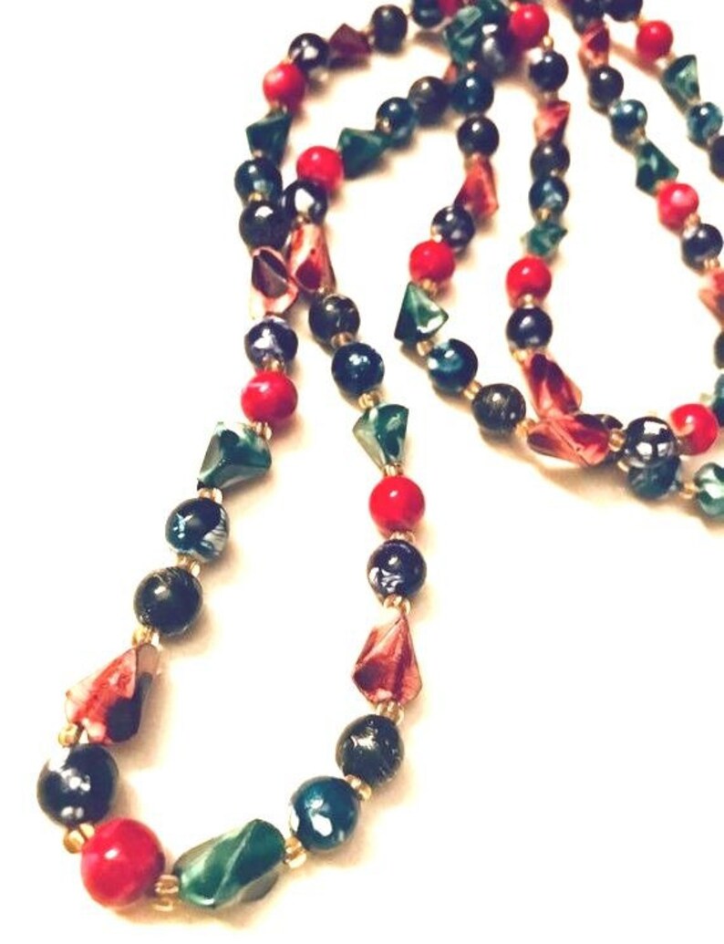 May include: A long necklace made of black, green, and red beads. The beads are various shapes and sizes, including round and triangular.