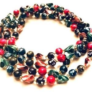 May include: Multi-strand necklace with black, green, and red beads. The beads are various shapes and sizes, including round, oval, and triangular.
