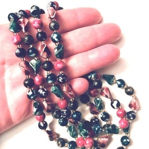 May include: A multi-strand necklace made of dark green, black, and pink beads. The beads are various shapes and sizes, including round, oval, and faceted.