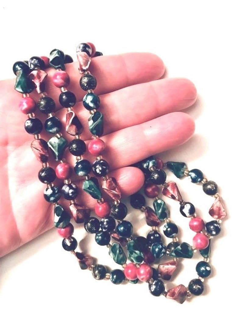 May include: A multi-strand necklace made of dark green, black, and pink beads. The beads are various shapes and sizes, including round, oval, and faceted.