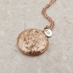 May include: Rose gold locket necklace with a floral design and a small heart charm. The locket is round and has a hinged lid.