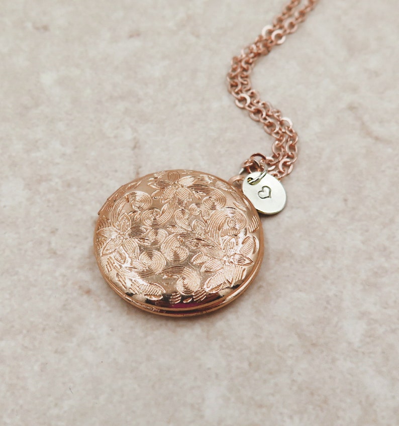 May include: Rose gold locket necklace with a floral design and a small heart charm. The locket is round and has a hinged lid.