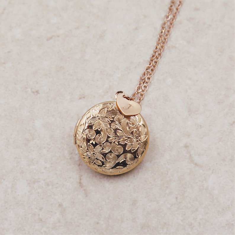 May include: Gold locket necklace with a floral design and a small heart charm with the letter 'J' engraved on it.