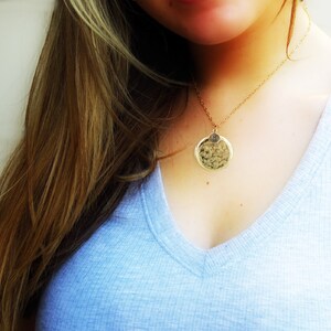 May include: A gold necklace with a round pendant featuring a textured design. The pendant has a small letter charm attached to it.