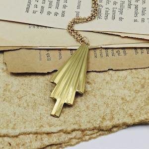 May include: A gold-toned necklace with a geometric, triangular pendant. The pendant has a textured, fan-like design.