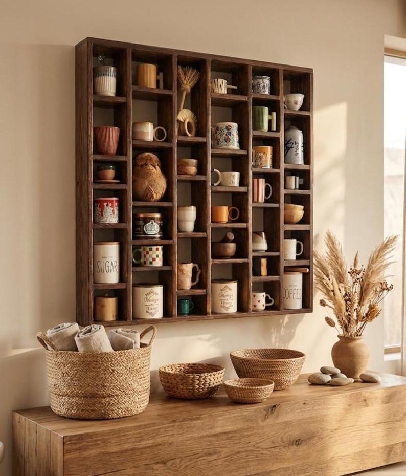 Pu&ograve; includere: Una mensola in legno scuro piena di varie tazze, piccole ciotole e oggetti decorativi. Sotto, un cesto intrecciato contiene asciugamani arrotolati e diverse ciotole intrecciate sono su una superficie di legno. Un vaso con piante secche &egrave; a destra.