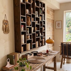 Pu&ograve; includere: Un tavolo in legno rustico con una collezione di libri, una pianta in vaso e una mensola decorativa piena di tazze e piccoli oggetti. Una lampada in stile vintage e un tappeto tessuto aggiungono all'estetica accogliente. La mensola &egrave; marrone scuro.