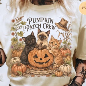 May include: An ivory t-shirt featuring a graphic of three kittens surrounding a carved jack-o'-lantern pumpkin. The design includes text that reads PUMPKIN PATCH CREW and AUTUMN ADVENTURE CLUB, surrounded by various pumpkins, corn stalks, and foliage.