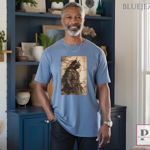 May include: A light blue t-shirt featuring a vintage-style illustration of a samurai warrior with a red sun in the background. The image includes Japanese text. The shirt is a solid color and has short sleeves.