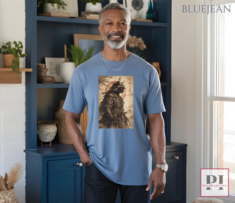 May include: A light blue t-shirt featuring a vintage-style illustration of a samurai warrior with a red sun in the background. The image includes Japanese text. The shirt is a solid color and has short sleeves.