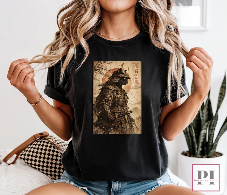 May include: Black t-shirt featuring a vintage-style graphic of a samurai cat in full armor, with a katana. The design includes a red sun and Japanese text. The shirt is a classic crew neck.