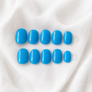 May include: A set of ten press-on nails in a vibrant, glossy sky blue colour. The nails are arranged in two horizontal rows of five, featuring a rounded oval shape with a smooth, reflective finish that highlights the bright blue pigment throughout.