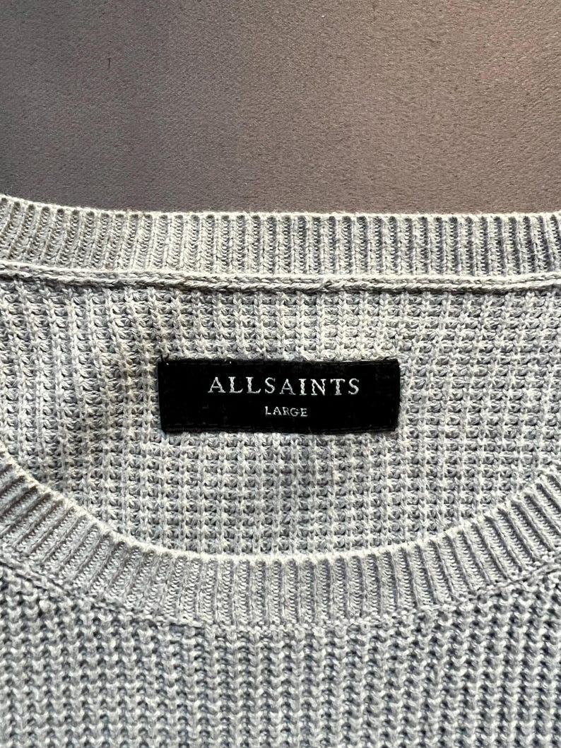 May include: A gray knitted sweater with a black label that reads "ALLSAINTS LARGE".