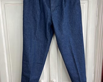 Puede incluir: Un par de pantalones de mezclilla azul oscuro con pliegues en la parte delantera. Los pantalones tienen cierre de botón y trabillas para el cinturón.