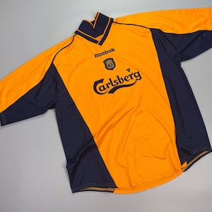 May include: An orange and navy blue soccer jersey with the Carlsberg logo and Reebok branding. The jersey has a V-neck collar and short sleeves. The jersey is made of a lightweight, breathable material.