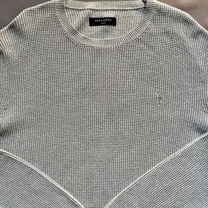 May include: A light blue waffle knit sweater with a small logo on the left chest. The sweater has a crew neck and long sleeves. The label on the sweater reads "AllSaints London".