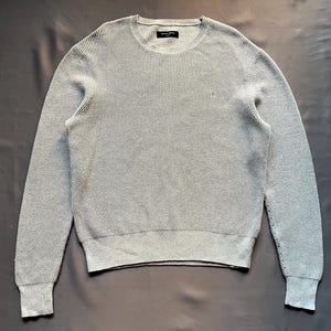 May include: A gray waffle knit sweater with a crew neck.