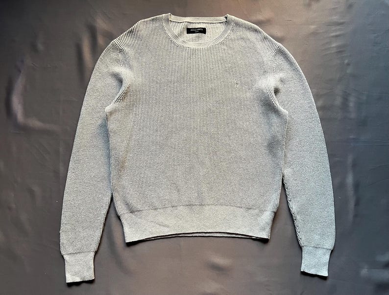 May include: A gray waffle knit sweater with a crew neck.