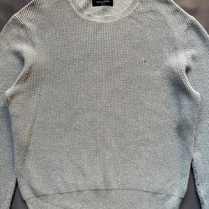 May include: A light gray waffle knit sweater with a small logo on the left chest. The sweater has a crew neck and long sleeves.