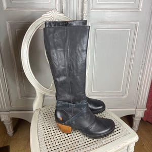 May include: Black leather knee-high boots with a wooden heel and a strap across the ankle.