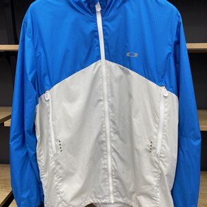 K&ouml;nnte beinhalten: Eine wei&szlig;e und blaue leichte Jacke mit Rei&szlig;verschluss und Kapuze. Die Jacke hat ein kleines Logo auf der Brust.