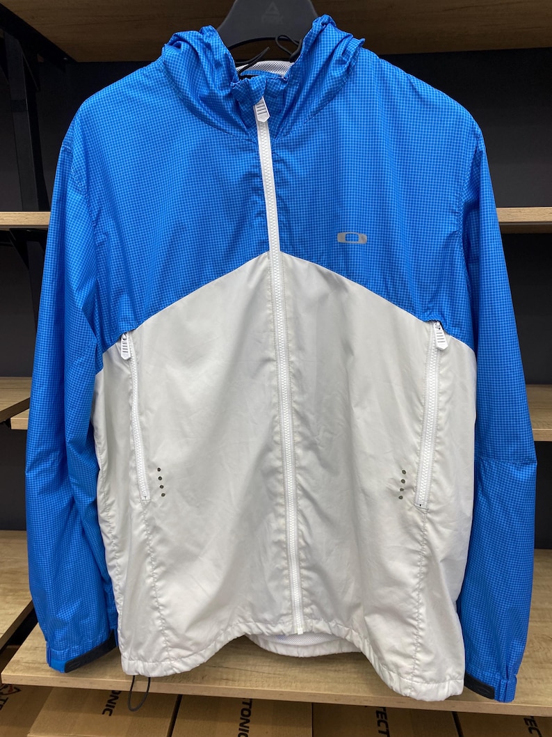 K&ouml;nnte beinhalten: Eine wei&szlig;e und blaue leichte Jacke mit Rei&szlig;verschluss und Kapuze. Die Jacke hat ein kleines Logo auf der Brust.