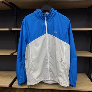 K&ouml;nnte beinhalten: Eine blaue und wei&szlig;e leichte Jacke mit Rei&szlig;verschluss und Kapuze. Die Jacke hat ein Logo auf der Brust, das "Oakley" sagt.