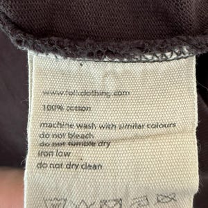May include: Close-up of a clothing tag with the text "www.folkclothing.com" and "100% cotton." The tag also includes washing instructions: machine wash with similar colors, do not bleach, do not tumble dry, iron low, and do not dry clean.