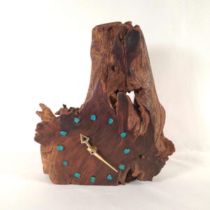 May include: A unique wooden clock carved from a tree trunk. The clock face is adorned with turquoise accents and gold-colored hands. The natural wood grain and texture create a rustic, artistic aesthetic.