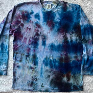 May include: A long-sleeved tie-dye shirt in shades of blue, purple, and white. The shirt has a crew neck and a relaxed fit. The tie-dye pattern creates a unique, abstract design. The shirt is made of a soft, comfortable material.