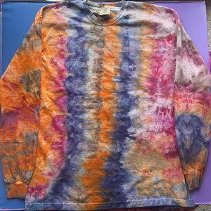 May include: A long-sleeved tie-dye shirt in a vibrant mix of colours. The shirt features a crew neck and a pattern of orange, purple, pink, and blue hues. The fabric appears soft and comfortable, suitable for casual wear.