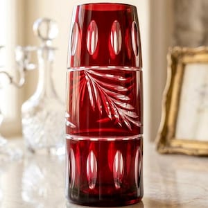 Può includere: Una pila di tre bicchieri di cristallo rosso rubino. Ogni bicchiere presenta un design ovale tagliato attorno alla parte superiore e inferiore, con un motivo a foglie inciso nel bicchiere centrale. I bicchieri sono impilati su una superficie di marmo.
