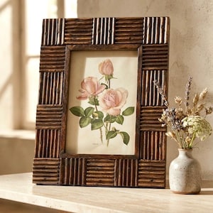 May include: A rectangular picture frame made of dark brown wood with a ribbed, textured border. The frame contains a botanical print featuring three light pink roses with green leaves and stems on a cream-colored background.