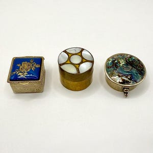 May include: Three decorative boxes. A square blue box with a gold floral design, a round box with a mother-of-pearl top, and a round box with an iridescent abalone shell top. All boxes have metal accents.