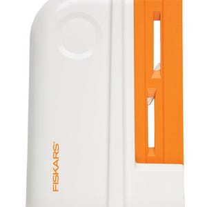 May include: A white and orange Fiskars vegetable slicer. The slicer has a white body with a rounded top and an orange section with slots. The Fiskars logo is printed in orange on the white body.