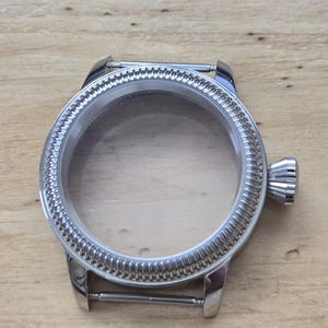Pu&ograve; includere: Una cassa dell'orologio color argento con un cristallo trasparente. La lunetta presenta un design strutturato e scanalato. La cassa dell'orologio ha una corona e anse per un cinturino. La cassa dell'orologio &egrave; vuota.