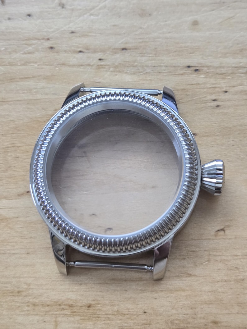 Pu&ograve; includere: Una cassa dell'orologio color argento con un cristallo trasparente. La lunetta presenta un design strutturato e scanalato. La cassa dell'orologio ha una corona e anse per un cinturino. La cassa dell'orologio &egrave; vuota.