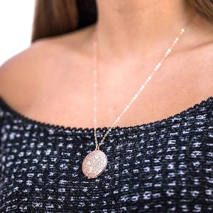 Op de afbeelding: Een vrouw draagt een zwarte off-shoulder trui met een delicate gouden kettingketting en een ronde, ros&eacute;gouden hanger.