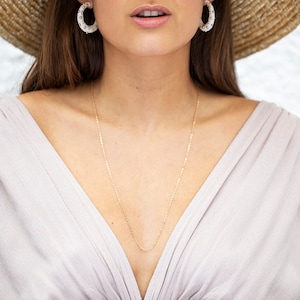 May include: A woman wearing a straw hat with a white top and a gold chain necklace. She is wearing white hoop earrings with gold accents.
