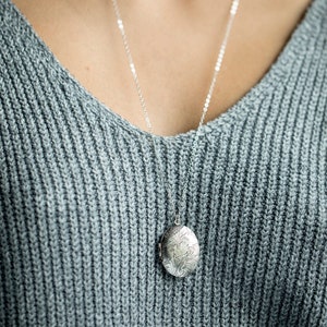 May include: A silver chain necklace with a silver locket pendant featuring an ornate floral design.