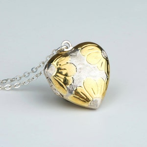 May include: A heart-shaped pendant necklace with a silver chain. The pendant is gold and silver, with a floral design. The necklace is on a white background.