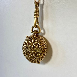 Puede incluir: Un collar de oro con un colgante redondo que presenta un intrincado diseño floral.