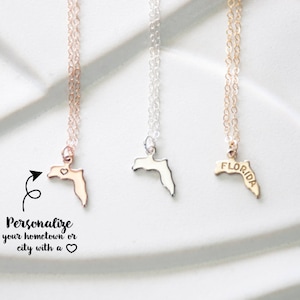 May include: Three gold necklaces with a Florida state outline pendant. The pendant on the left has a small heart inside the outline. The pendant in the middle is plain. The pendant on the right has the word "FLORIDA" inscribed on it.