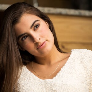 May include: A young woman with long brown hair wearing a white fuzzy sweater and a gold chain necklace. She is looking up and to the right.